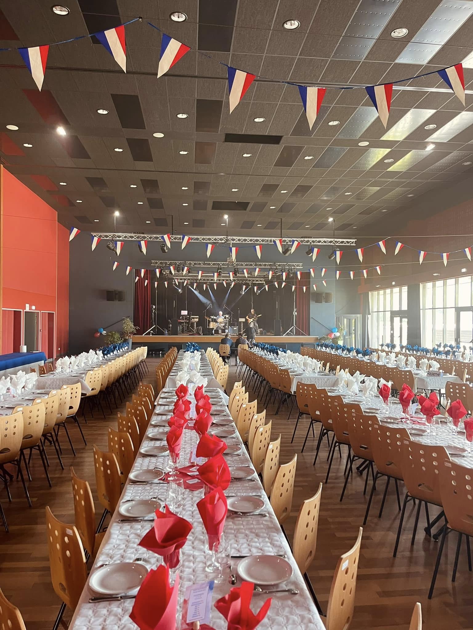 Salle des fêtes décorée, tables dressées face à la scène